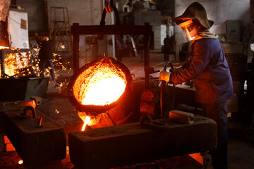 Industrial worker pours molten metal at foundry. Steel production in heat-resistant suit, helmet....