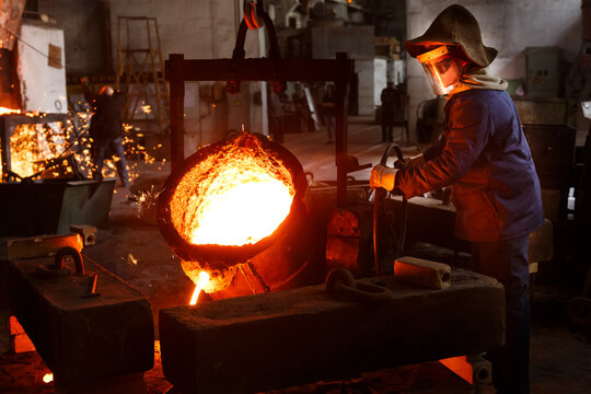 Industrial worker pours molten metal at foundry. Steel production in heat-resistant suit, helmet. Heavy industry labor. Metallurgy process, smelting iron in blast furnace. Metalwork, hot iron casting.