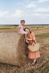 Mom and little daughter in a field of harvested wheat against the blue sky. Mom rested her cheek on her little daughter's knee