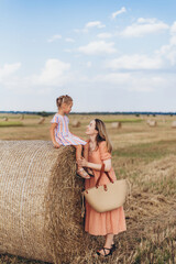 Mom and little daughter in a field of harvested wheat against the blue sky. Mom and daughter look into each other's eyes