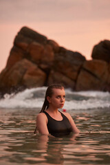 Fototapeta premium Woman relaxes in sea at sunset. Tranquil marine swim, wellness leisure activity. Fit female in swimsuit enjoys natural water, serenity at dusk. Harmony with ocean, healthy beach lifestyle. Solo travel