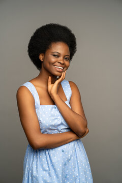 Charismatic merry dark skinned african female with natural curly hair, unusual white teeth, smiling with cheek dimples. Optimistic female wearing summer dress, isolated on grey studio background
