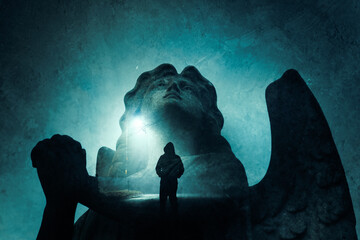 A double exposure of a graveyard angel statue praying. With a spooky hooded figure.  Standing on a...