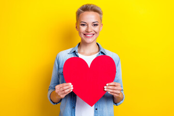 Photo portrait of attractive young woman hold big red heart postcard dressed stylish denim clothes isolated on yellow color background