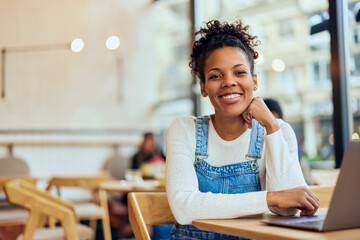 Portrait of a smiling African woman sitting at the cafe and using a laptop.