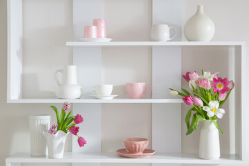 Fototapeta na wymiar tulips in vase on white shelf with kitchenware