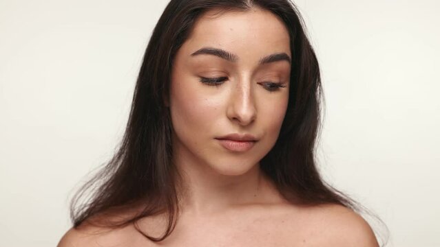 Close-up image capturing the natural beauty and calm expression of a young brunette woman with neutral makeup against a soft white backdrop.