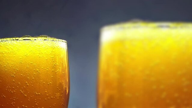 Orange soda is pouring into a two glasses with ice cubes on a white wall background. Overflowing wet 2 glasses with pop orange soda. 4k macro video with speed ramp effect.