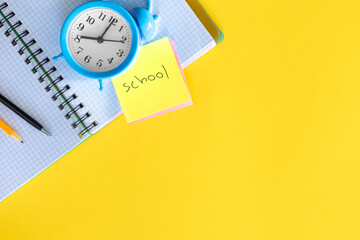 Alarm clock, notepad and the inscription School on a paper sticker, flat lay.