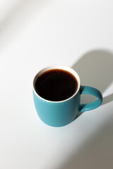 A cup of coffee stands on a white background with a shadow from the window in the morning light