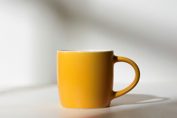 A cup of coffee stands on a white background with a shadow from the window in the morning light