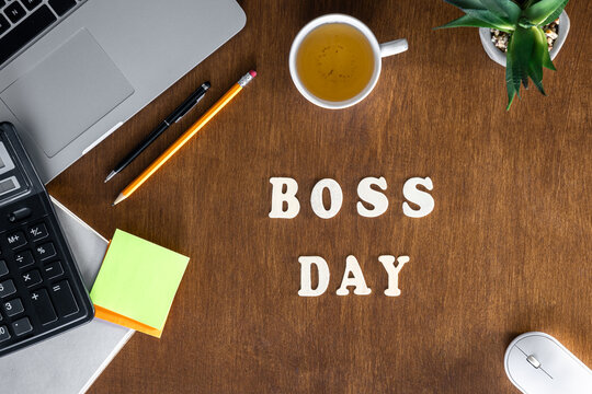 Wooden inscription Boss Day on a wooden office desk background, top view.