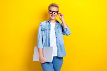 Photo portrait of lovely young lady touch specs hold netbook dressed stylish denim garment isolated on yellow color background