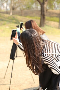 Ladies taking pictures with smartphones in the park
