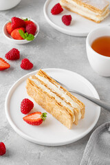 Traditional French dessert millefeuille with vanilla cream and fresh berries on a white plate on a gray concrete background.