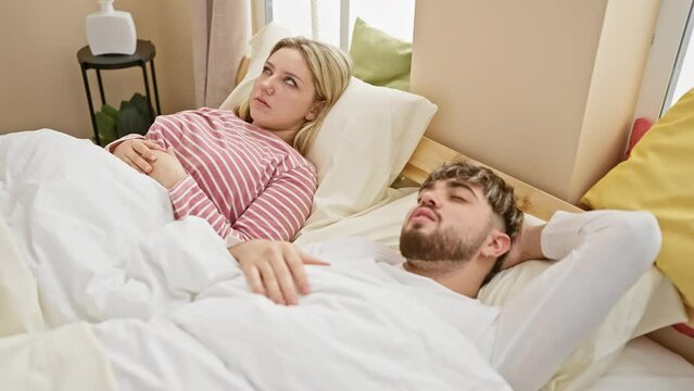 Awake woman annoyed by snoring man in a cozy bedroom setting, reflecting couple sleep issues. - Powered by Adobe