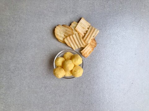Hand holding Crispy corrugated potato chips or potato chips and Cheese Corn balls. Junk food. Close up. Keripik Singkong or Keripik Kentang dan snack bulat
