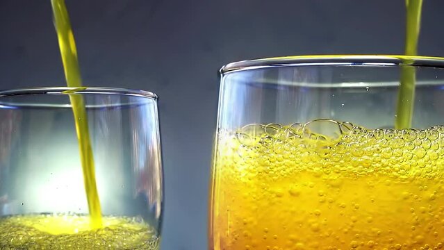 Orange soda is pouring into a two glasses with ice cubes on a white wall background. Overflowing wet 2 glasses with pop orange soda. 4k macro video 60 fps.
