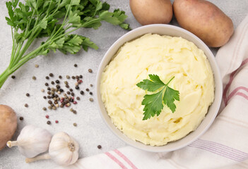 Bowl of tasty mashed potato, parsley,  and pepper on grey marble table