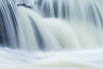 Winter landscape of the Rabbit River Cascade framed by ice and captured with motion blur, Michigan,...