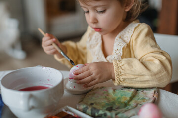 Close-up of a cute little girl painting eggs for Easter at a table. Easter family traditions.