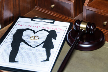 A clipboard holding a prenuptial agreement with a cut-out silhouette of a couple and wedding rings,...