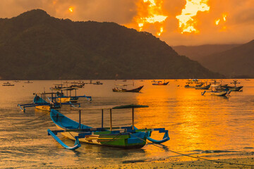 A group of colorful boats docked on a calm lake at sunset, with mountains and clouds in the background.