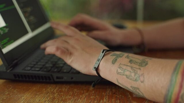 Programmer types code on laptop, fingers rapidly pressing keys. In focus coding on screen, tattooed hands typing. Web development, cyberspace workflow. Slow motion.