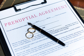 Close-up of a prenuptial agreement form with wedding rings and a fountain pen, indicating the legal...
