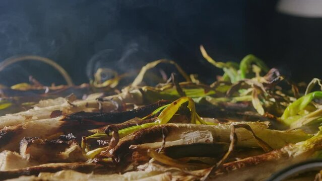 Traditional Spanish catalan green winter onion calcots, spring green season grill barbecue, vegan bbq with fire in Barcelona, Catalonia. Close up of grilling green onion.
