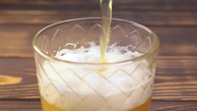 Full glass with beer head to the very top. Pouring liquid gold-yellow beer with white foam into a glass. Close up view. Slow motion.