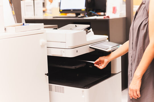 Woman officer pull printing paper document out from functional office printer.