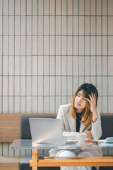 Stressed businesswoman at a cafe with laptop, showing signs of fatigue or headache during a busy...