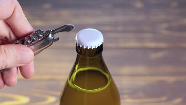 Metal corkscrew is opening of beer Bottle. Opener with cap, close up. Slow motion.