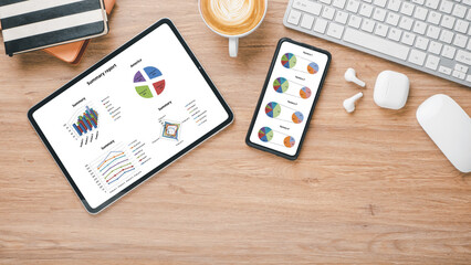 Workspace with tablet and smartphone displaying colorful pie charts and graphs for business...