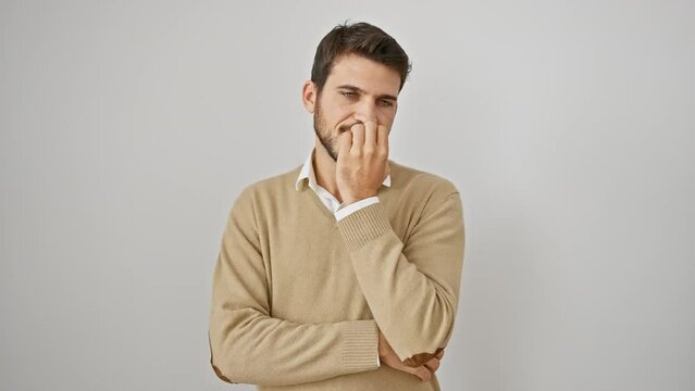 Portrait of a young hispanic man wearing a sweater, looking stressed and nervous. anxiety ridden, he stands alone biting his nails, hands near his mouth on a stark, isolated white background.