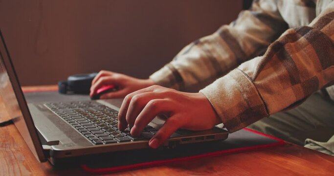 Close up of teenager's hands fluently fingering laptop keys and using mouse. Cybersport