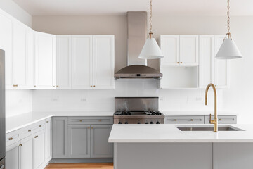 A kitchen detail with grey and white cabinets, gold faucet, gold and white pendant lights hanging...
