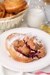 Delicious bun with sugar powder and berries on table, closeup