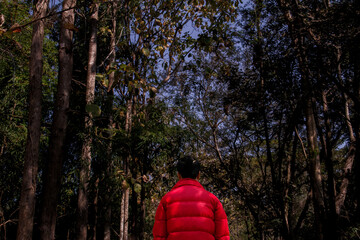 A man wearing red shirt standing before the dark forest background