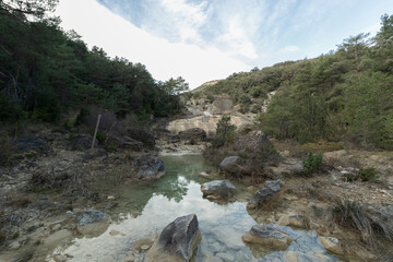 a tranquil natural landscape with a clear pond, surrounded by rocky terrain and lush greenery under...