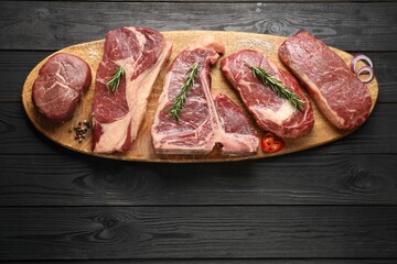 Pieces of raw beef meat and spices on black wooden table, top view. Space for text