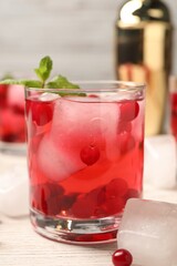 Tasty cranberry cocktail with ice cubes in glass on wooden table