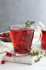 Tasty hot cranberry tea with thyme and fresh berries in glass cup on white wooden table