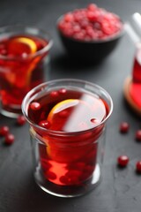 Tasty hot cranberry tea with lemon and fresh berries in glass on black textured table