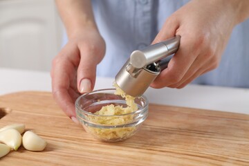 Woman squeezing garlic with press at wooden table indoors, closeup - obrazy, fototapety, plakaty