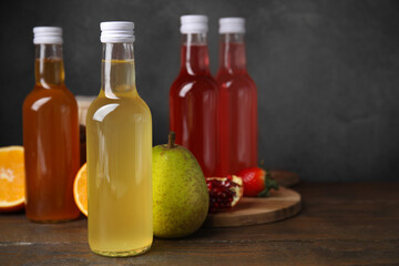 Delicious kombucha in glass bottles and fresh fruits on wooden table, space for text