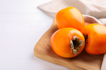 Board with delicious ripe persimmons on white wooden table, closeup. Space for text