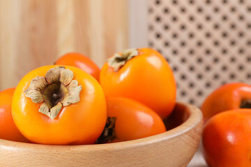 Delicious ripe persimmons in bowl on blurred background, closeup