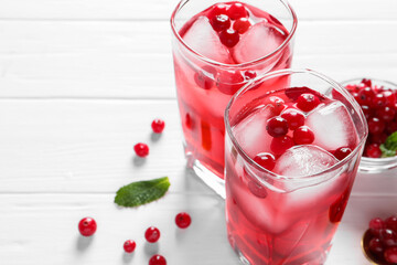 Tasty cranberry juice with ice cubes in glasses and fresh berries on white wooden table, closeup. Space for text